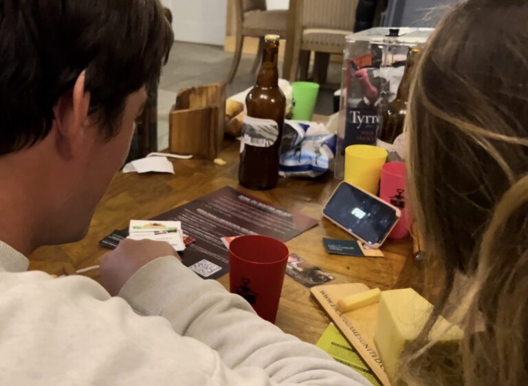Deux amis penchés sur les indices et cartes du jeu "Escape Games L'Apéro" autour d'une table