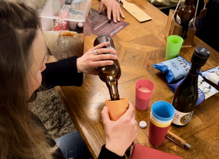 Joueuse versant une bière dans un gobelet du kit "Escape Games L'Apéro" entourée de chips et de vin