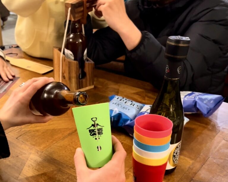 Bouteille de bière et gobelets colorés du kit "Escape Games L'Apéro" sur une table en bois