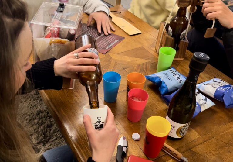 Joueuse versant une bière dans un gobelet marqué "Escape Games" entourée de chips et de vin