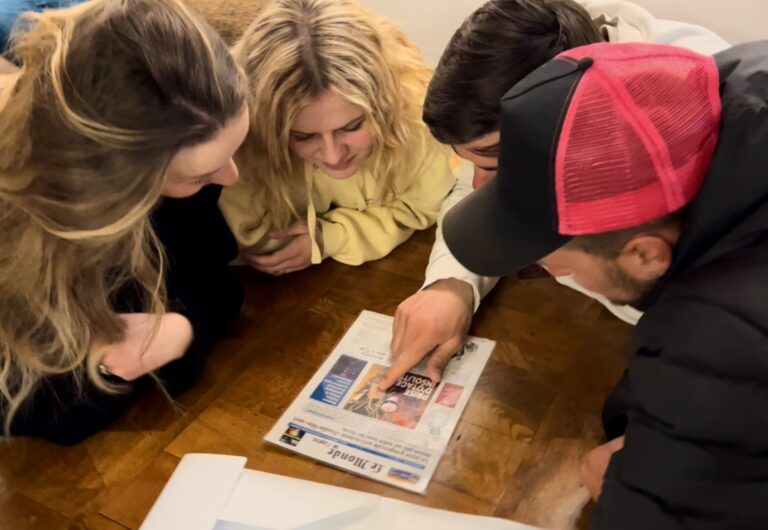 Groupe d'amis assis autour d'une table en bois, penchés sur un indice de jeu "Escape Games L'Apéro"