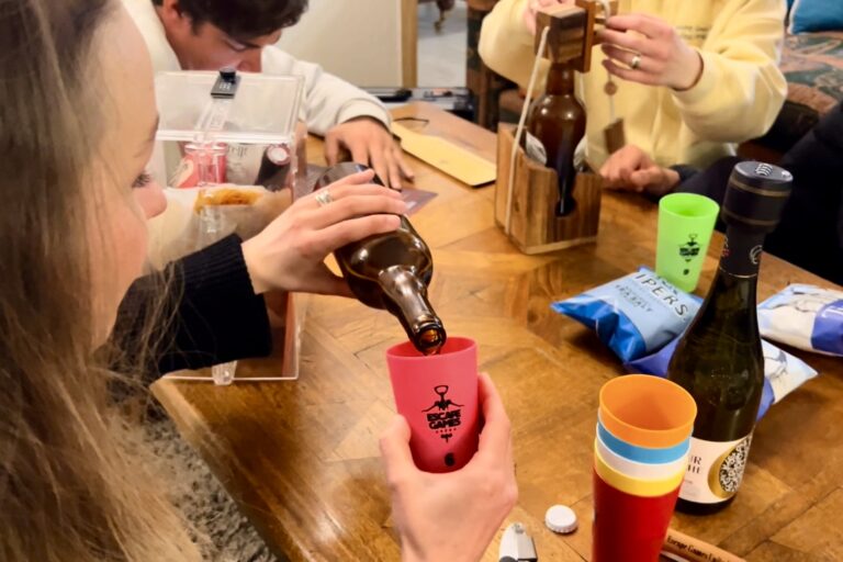 Joueuse versant une bière dans un gobelet rose "Escape Games" entourée d'accessoires du jeu