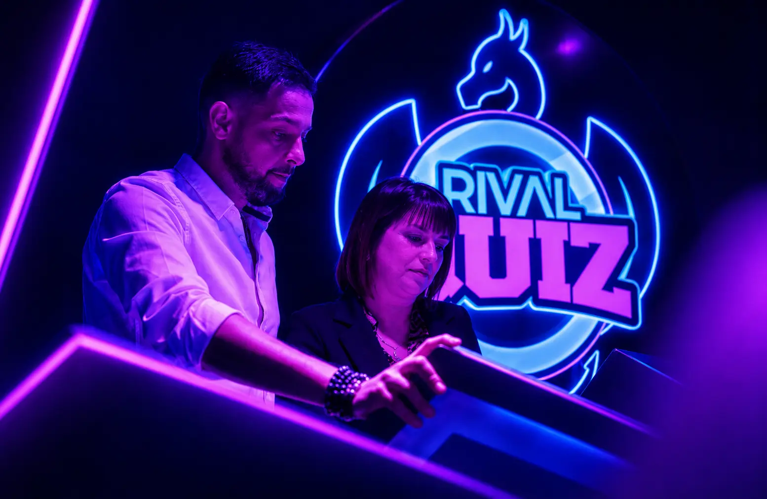 Un animateur Virtual Arena aide une joueuse sur le pupitre du jeu Rival Quiz aux néons violets