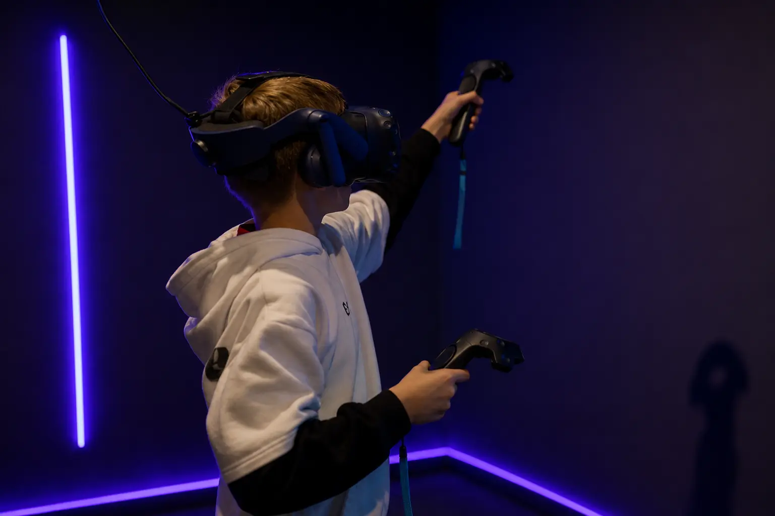 Adolescent équipé d'un casque VR levant le bras avec sa manette lors d'un escape game en réalité virtuelle